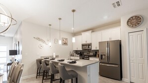 A modern kitchen with a central island, bar stools, stainless steel appliances, and pendant lighting. - 230oca - The Retreat at Championsgate (Kissimmee)