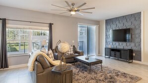 A modern living room with a sofa, coffee table, globe, and TV. - 230oca - The Retreat at Championsgate (Kissimmee)