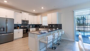 A modern kitchen with white cabinets, stainless steel appliances, a central island with bar stools, and a view of a swimming pool through large windows. - 4569tb NON Renting 09/13/2021 -storey Lake (Kissimmee)