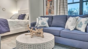 Ein modernes Wohnzimmer mit grauem Sofa, einem runden Couchtisch mit dekorativem Mittelstück und einem Bett mit gemusterten Betttextilien.