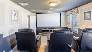 Un cine en casa con tres sillones de cuero reclinables, un televisor de pantalla plana grande y un mueble de entretenimiento de madera.