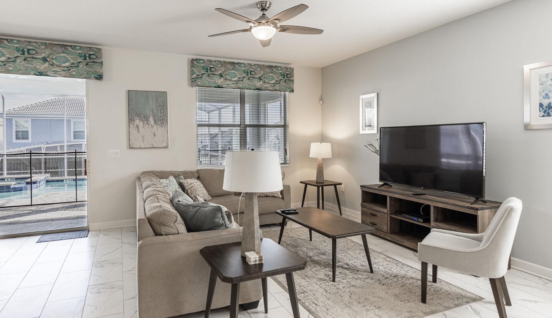 A living room with a sofa, coffee table, TV stand, and a ceiling fan.