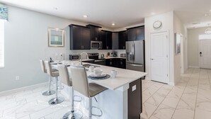 Una cocina moderna con armarios oscuros, electrodomésticos de acero inoxidable y una isla central con taburetes de bar.
