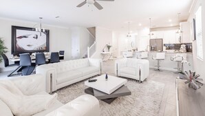 Un salon moderne avec un canapé blanc, une table basse et un coin repas agrémenté d’un lustre.
