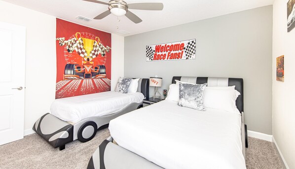 A hotel room with two beds, a racing-themed wall art, a welcome sign, and a ceiling fan.