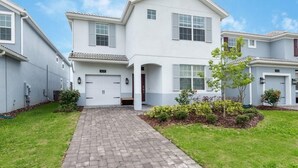 A two-story residential building with a paved driveway, a small front yard with shrubs, and a clear sky. - C1614mvd-the Retreat at Championsgate (Davenport)