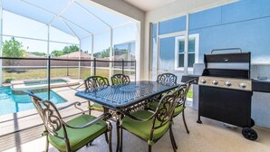 A covered patio with a pool, a grill, and a table with chairs. - C1614mvd-the Retreat at Championsgate (Davenport)