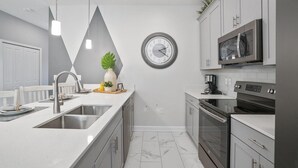 Een moderne keuken met een wit aanrechtblad, roestvrijstalen apparatuur en een klok aan de muur.