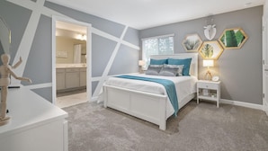 Een slaapkamer met een bed, nachtkastje en een bedtafel. Er is een spiegel, een raam met jaloezieën en een deur die leidt naar een andere kamer.