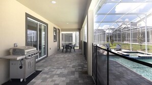 Un patio abrité avec un barbecue, une piscine et une vue sur une maison.