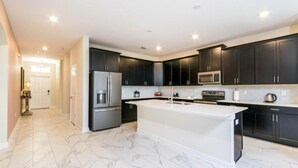 A modern kitchen with dark cabinets, a large island, stainless steel appliances, and marble flooring. - C1573fd-the Retreat at Championsgate (Davenport)