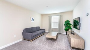 A living room with a gray sofa, a wooden coffee table, a wooden cabinet, and a large green plant. - C1573fd-the Retreat at Championsgate (Davenport)