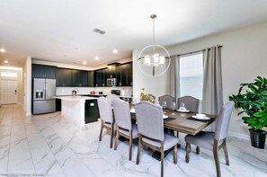 A modern kitchen with dark cabinets, a central island, and a dining area with a chandelier. - C1573fd-the Retreat at Championsgate (Davenport)