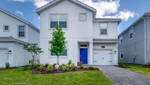 A modern two-story residential building with a blue front door, a small tree in the front yard, and a paved driveway. - C1573fd-the Retreat at Championsgate (Davenport)