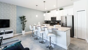 A modern kitchen with white cabinets, stainless steel appliances, and a central island with bar stools. - 4815ds-non Renting February 1, 2023 Storey Lake (Kissimmee)