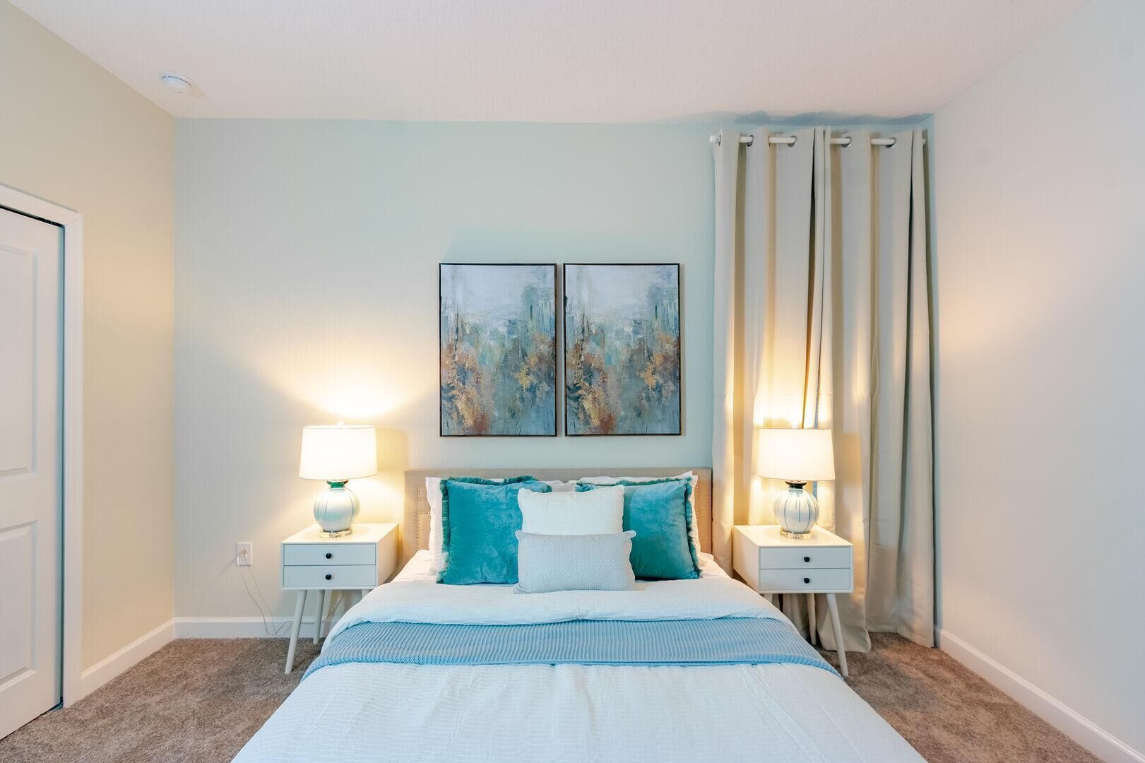 Een slaapkamer met een bed, twee nachtkastjes, twee lampen en twee abstracte schilderijen aan de muur.
