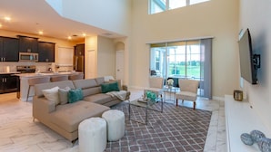 A spacious living area with a sectional sofa, ottomans, a coffee table, and a view of the outdoors through large windows.