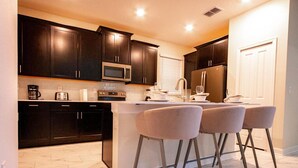 A modern kitchen with dark cabinets, a microwave, a refrigerator, and a bar area with three stools.