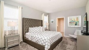 A bedroom with a large bed, bedside tables, a dresser, a desk, and a chair. There are two windows with curtains, a door, and a painting on the wall. - 1533mc -non-renting The Retreat at Championsgate (Davenport)