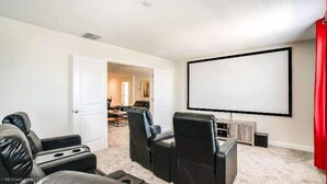 A home theater room with a large screen, leather recliner seating, and carpeted flooring. - 1533mc -non-renting The Retreat at Championsgate (Davenport)