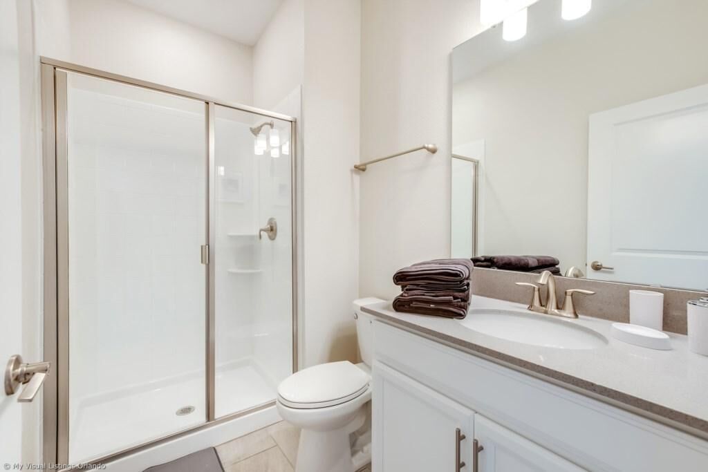 A modern bathroom with a glass shower enclosure, a white toilet, and a vanity with a sink and mirror.