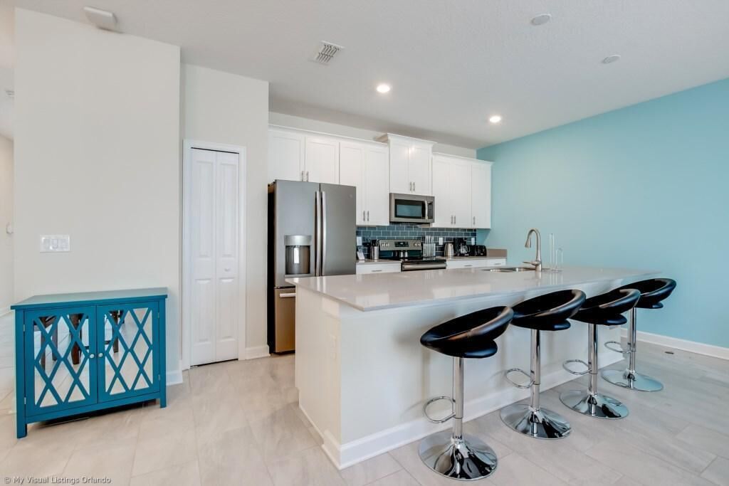 Une cuisine moderne avec des meubles blancs, un îlot central doté de tabourets de bar et un élément décoratif de couleur turquoise.