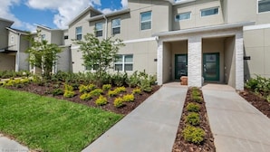 A modern residential building with a central entrance, a covered porch, and a landscaped front yard with shrubs and a lawn. - C800pbd - The Retreat at Championsgate (Davenport)