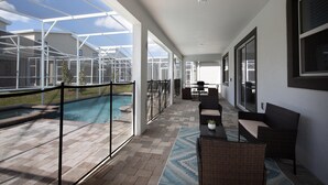 A covered outdoor area with a pool, seating, and a view of the sky. - 840dsd-the Retreat at Championsgate (Kissimmee)