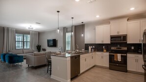 A modern kitchen with white cabinetry, a central island, stainless steel appliances, and pendant lighting. - 840dsd-the Retreat at Championsgate (Kissimmee)