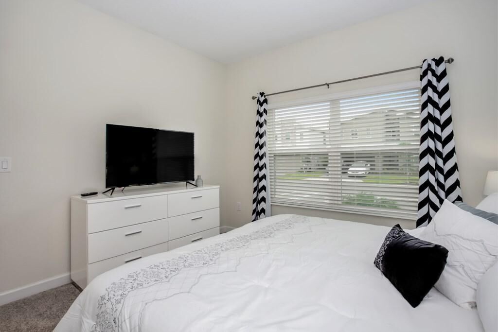 A bedroom with a bed, a TV on a dresser, and a window with blinds.