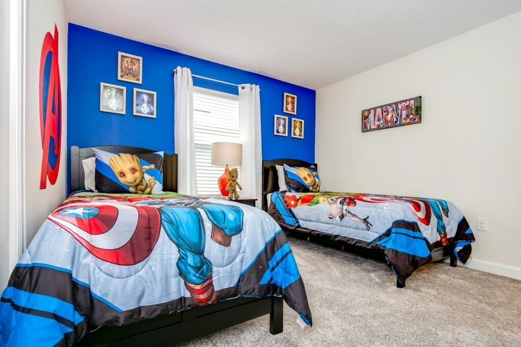 A bedroom with two beds, each covered with superhero-themed bedding.