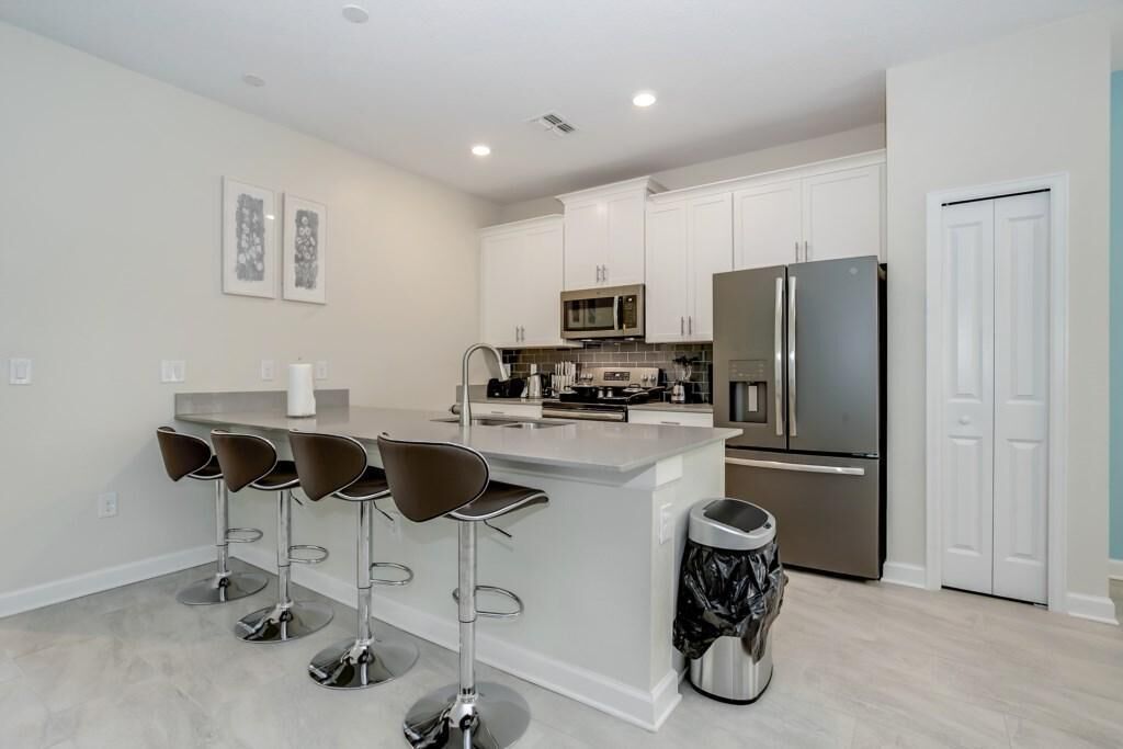 A modern kitchen with white cabinets, stainless steel appliances, and a central island with bar stools.