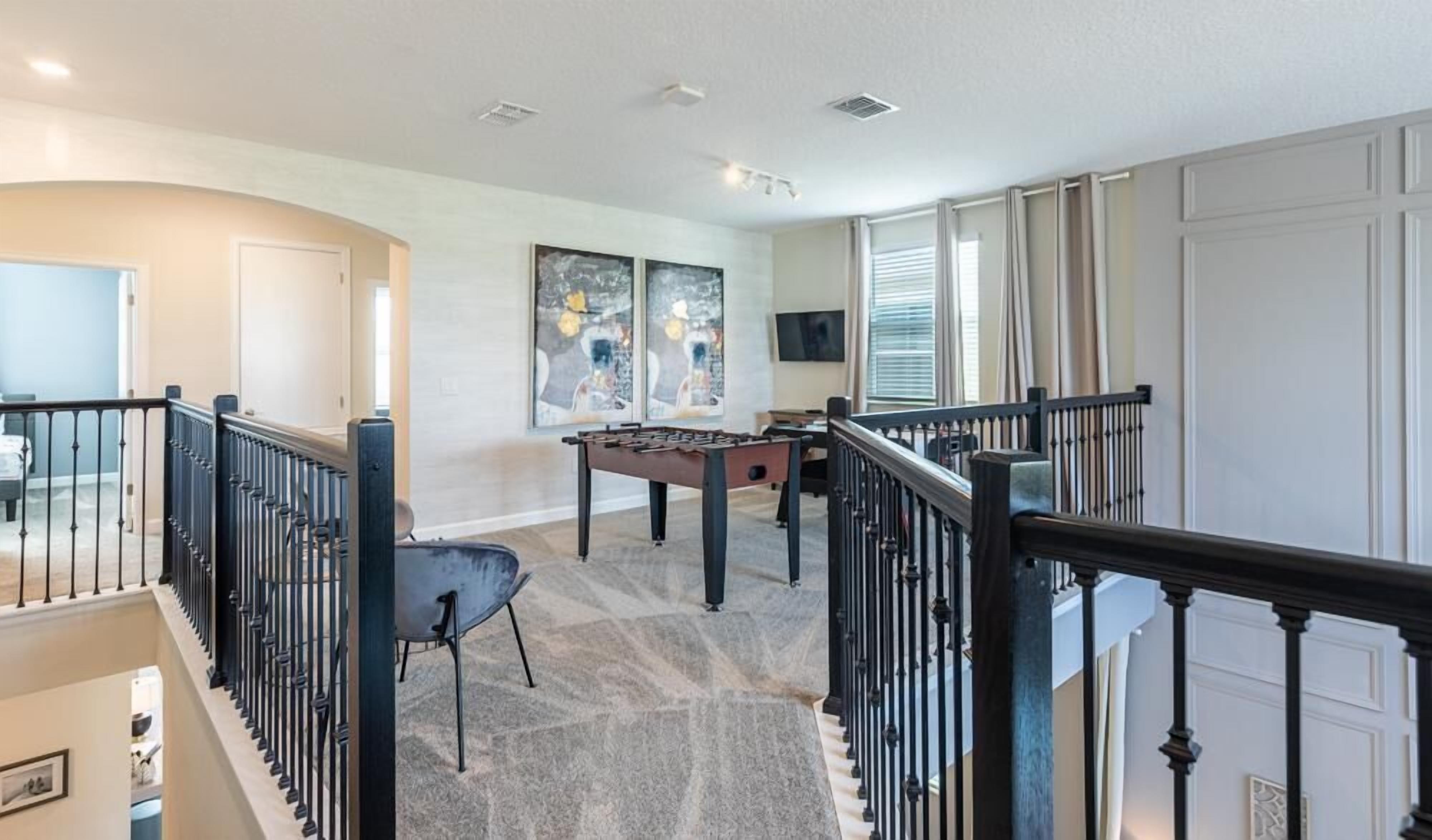 Un grand espace de vie comprenant une table de baby-foot, un coin salon confortable et un escalier avec une rampe.