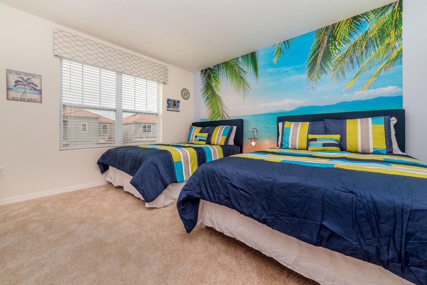 Un dormitorio con dos camas, un mural con motivos playeros, una ventana con persianas y suelo alfombrado.