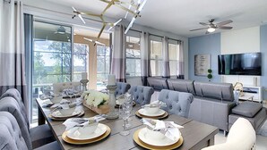 A modern dining area with a long table set for a meal, a comfortable seating area with sofas, and a television mounted on the wall. - 8043osc-solterra Resort (Davenport)