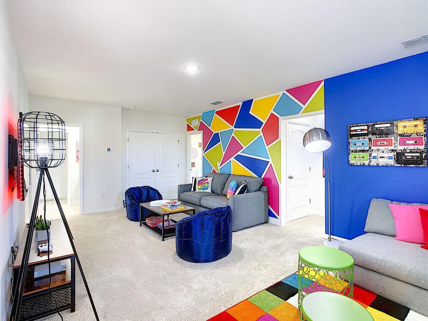 A modern living room with a colorful geometric wall design, a grey sofa, a blue armchair, and a small coffee table.