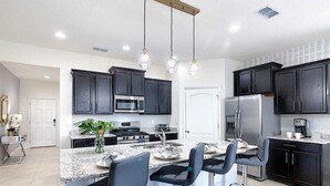 A modern kitchen with dark cabinets, stainless steel appliances, and a central island with bar stools. - 8043osc-solterra Resort (Davenport)