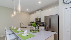Una cocina moderna con armarios blancos, electrodomésticos de acero inoxidable y una isla grande con individuales verdes y servilletas blancas.