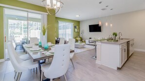 Una cocina moderna con armarios blancos, una zona de comedor con sillas blancas y un ventanal grande.