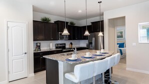 A modern kitchen with dark cabinets, a granite countertop, and a bar area with white stools. - 8912prw- NON Renting July 7, 2022 Windsor at Westside (Kissimmee)