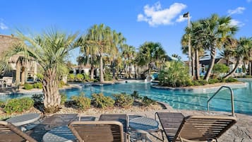 A pool area with lounge chairs, palm trees, and a water slide.