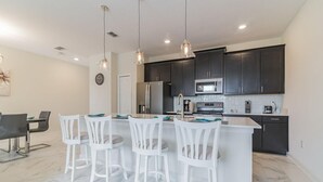 A modern kitchen with dark cabinets, a stainless steel refrigerator, a microwave, and a stove. There are four white bar stools around a central island. - 560pb- The Retreat at Championsgate (Davenport)