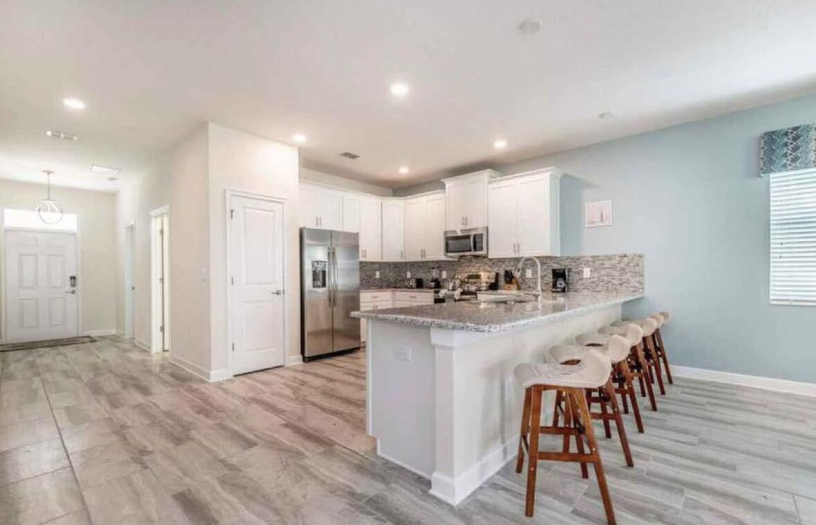 A modern kitchen with white cabinets, a large island with bar stools, stainless steel appliances, and a light blue accent wall.