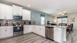 A modern kitchen with white cabinets, a granite countertop, stainless steel appliances, and a central island. - C9036sid-the Retreat at Championsgate (Davenport)