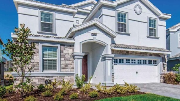 A two-story house with a stone facade, a garage, and a well-maintained front yard. - C9036sid-the Retreat at Championsgate (Davenport)