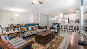 A spacious living room with a sofa, coffee table, and a dining area with chairs. There is a kitchen in the background with a refrigerator and a microwave. - C9036sid-the Retreat at Championsgate (Davenport)
