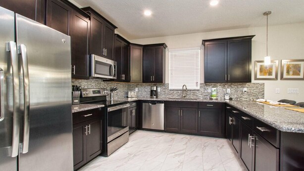 A modern kitchen with dark cabinets, stainless steel appliances, a granite countertop, and a window with blinds. - 9032hs-the Retreat at Championsgate (Davenport)