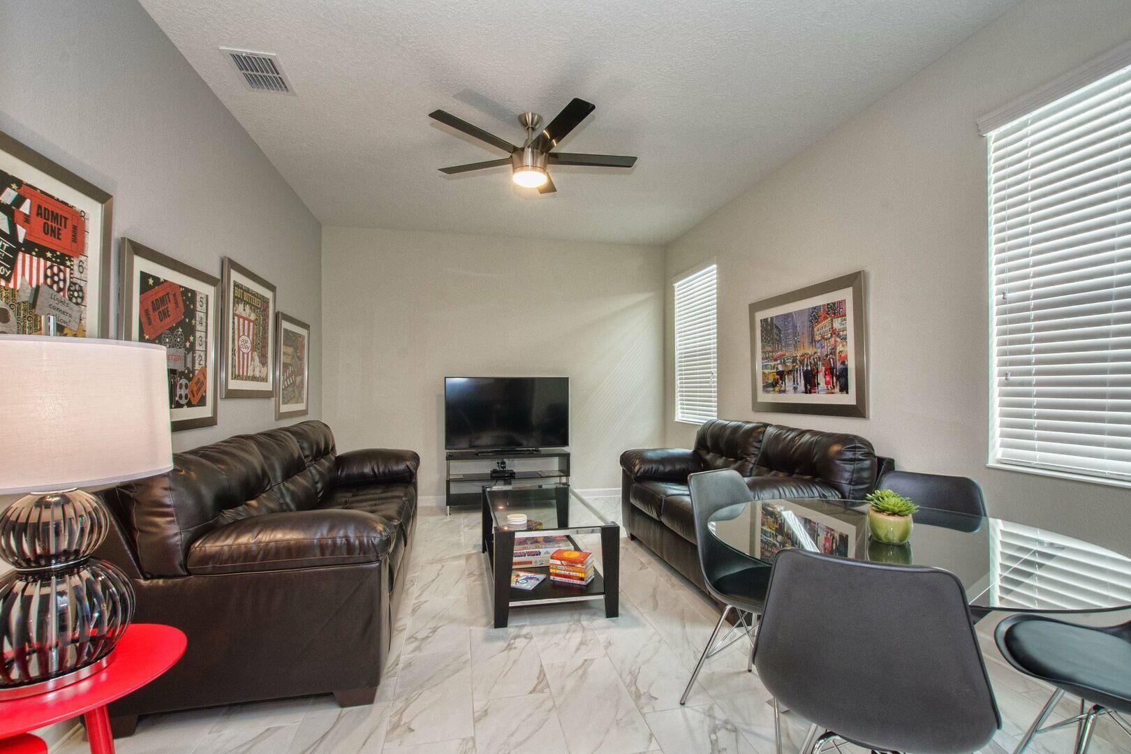 A living room with two leather sofas, a glass coffee table, a TV, and framed pictures on the walls.