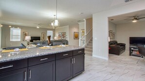 A spacious living area with a large kitchen island, dark cabinetry, and a modern chandelier. - 9032hs-the Retreat at Championsgate (Davenport)