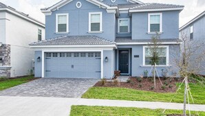 A two-story residential house with a garage, a front yard with a small tree, and a clear sky. - 9032hs-the Retreat at Championsgate (Davenport)